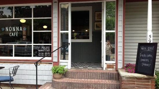 The storefront of Nonna's Cafe. There is an open door with the view of black and white checkered flooring, leading out to three brick steps and outdoor seating. 