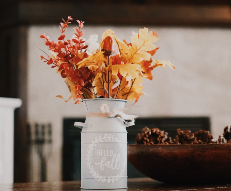 Fake maple leaves, acorns, and yellow leaves in a matte white vase next to a bowl of acorns